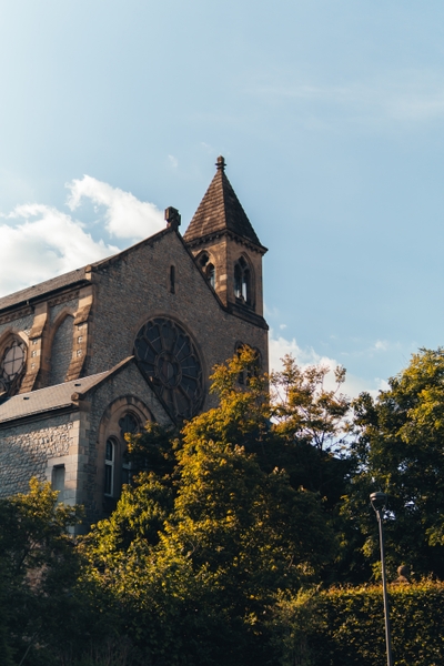 Église en pierre avec clocher pointu et arbres autour
